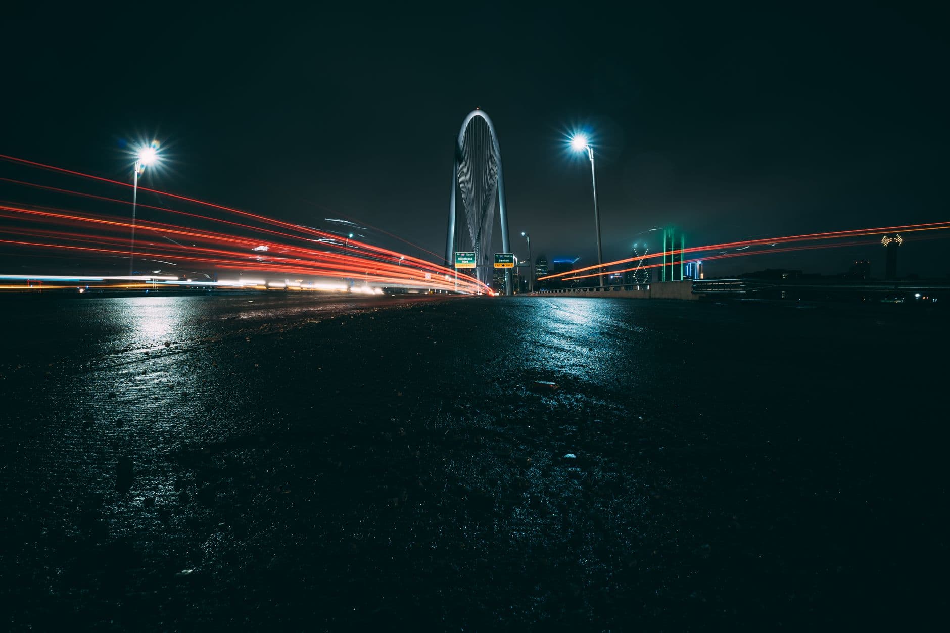 Dramatic long-exposure of Dallas bridge with car lights streaking under a night sky.